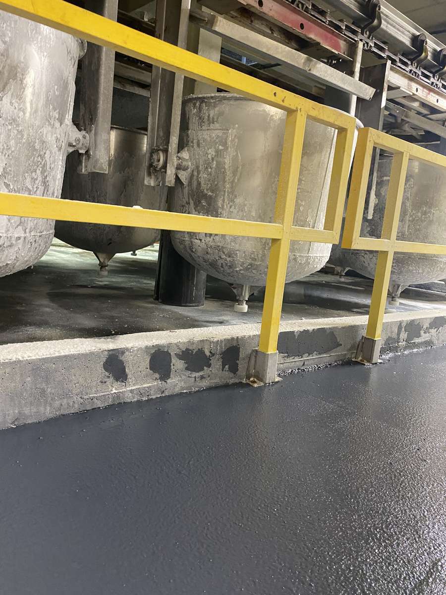 Resinous floor beside process vessels and a yellow safety railing